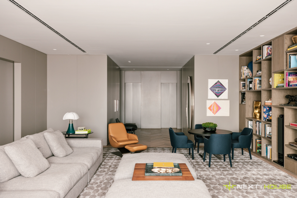 Ambiente de estar sofisticado com sistema de áudio e vídeo integrado à arquitetura, poltrona de couro caramelo e estante de marcenaria com caixa acústica de coluna, projeto NEXTTHOUSE.